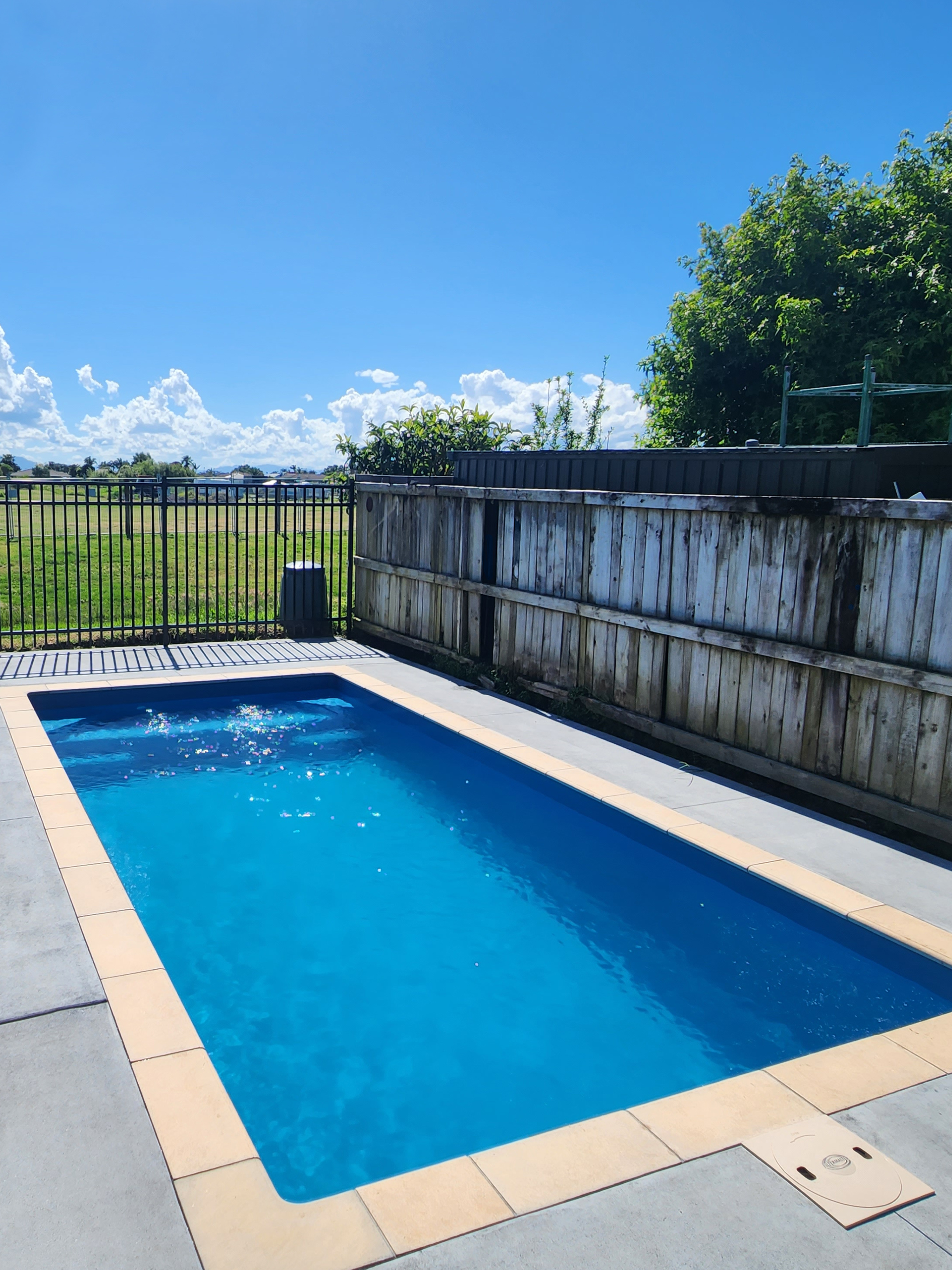 Beach Blue fibreglass pool with mid blue water and timber fence