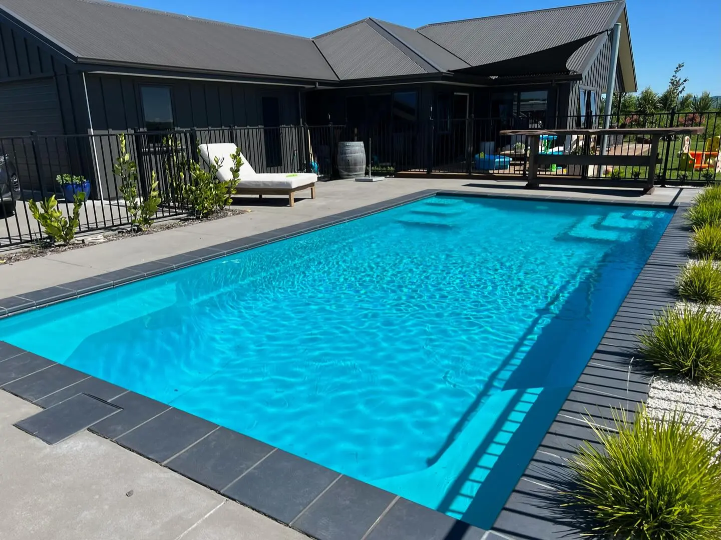 A Bayside Horizon pool in a finished backyard, loungers on the paving and the house behind